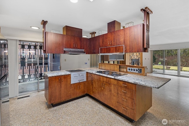 kitchen featuring light speckled floor, gas stovetop, visible vents, a peninsula, and under cabinet range hood