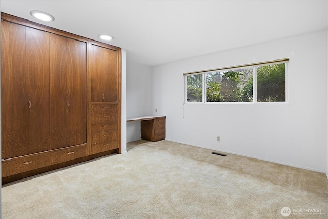 unfurnished bedroom featuring recessed lighting, light colored carpet, visible vents, a closet, and built in study area