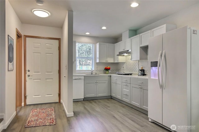 kitchen with white appliances, a sink, light countertops, under cabinet range hood, and light wood-type flooring