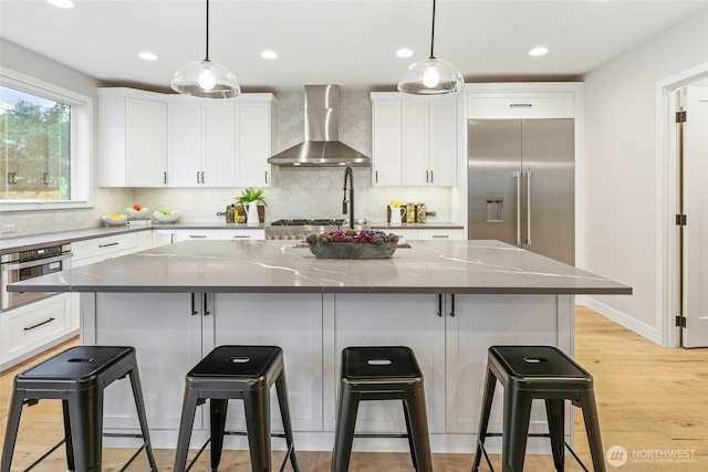 kitchen featuring wall chimney exhaust hood, stainless steel appliances, hanging light fixtures, and a center island