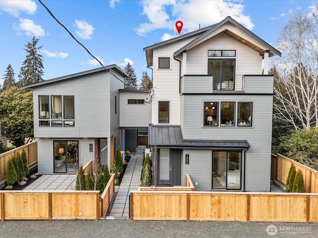 rear view of house with a balcony, fence private yard, metal roof, and a standing seam roof