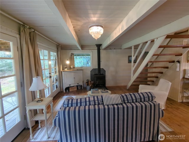 living room featuring a wood stove, french doors, beamed ceiling, and light wood-type flooring