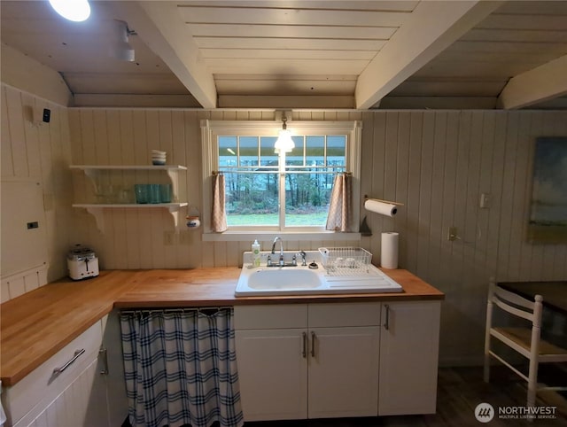 bathroom featuring beam ceiling, sink, and wooden walls