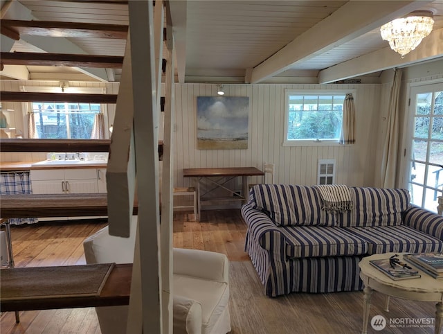 living room with sink, a notable chandelier, light wood-type flooring, wooden walls, and beam ceiling