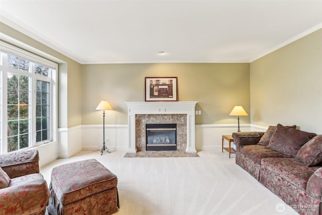 living room featuring light colored carpet, a premium fireplace, baseboards, wainscoting, and crown molding