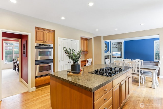 kitchen with black gas cooktop, double oven, light wood-type flooring, and a center island