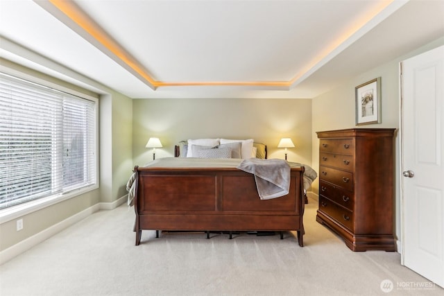 bedroom featuring light carpet, baseboards, and a raised ceiling