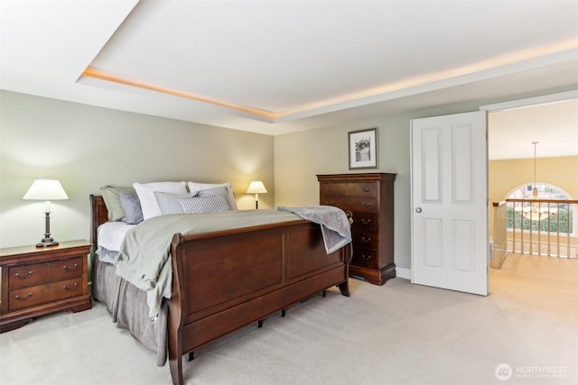 bedroom with a chandelier, a tray ceiling, and light colored carpet