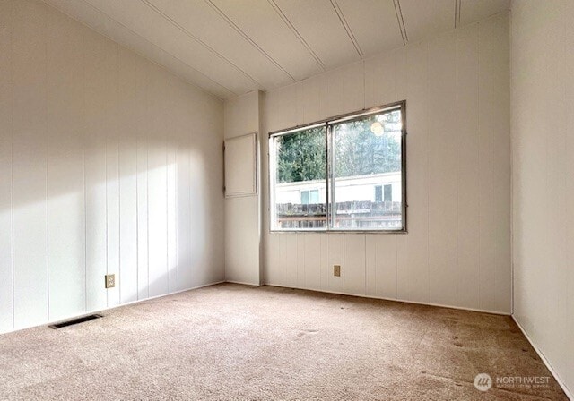 carpeted spare room featuring visible vents and vaulted ceiling