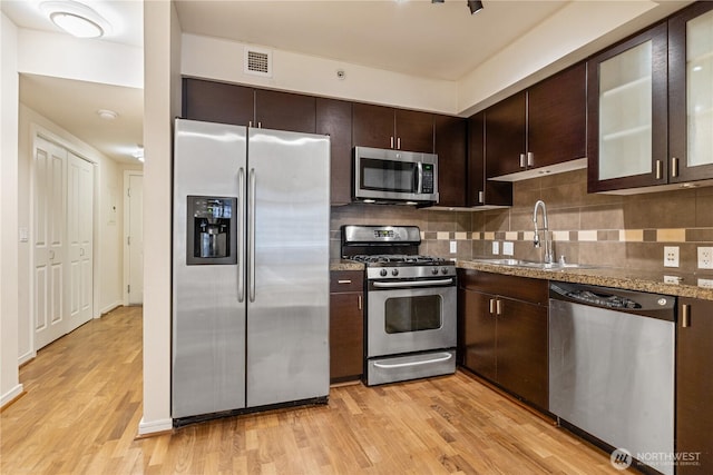 kitchen with sink, light stone countertops, light hardwood / wood-style floors, stainless steel appliances, and dark brown cabinetry