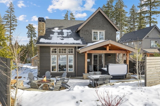 snow covered back of property featuring a chimney, fence, a fire pit, and a patio