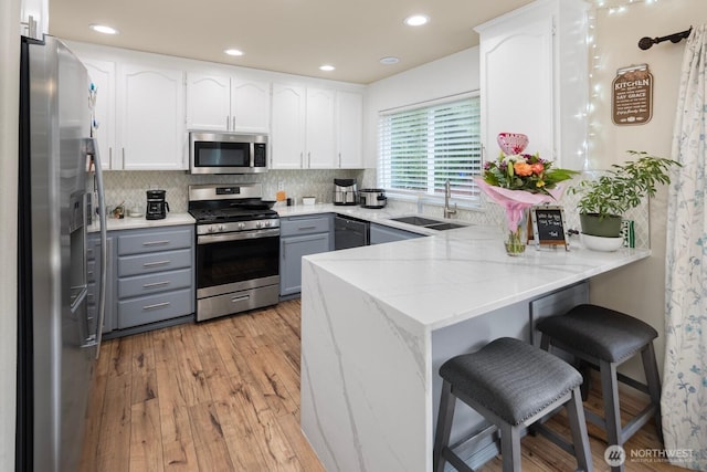 kitchen featuring white cabinets, appliances with stainless steel finishes, a peninsula, gray cabinetry, and a sink