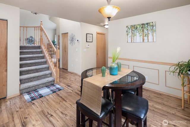 dining room with light wood finished floors, stairway, wainscoting, and a decorative wall