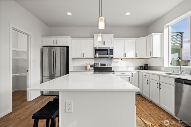 kitchen with a sink, white cabinets, light countertops, appliances with stainless steel finishes, and a center island