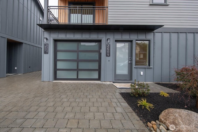 doorway to property featuring a balcony, an attached garage, decorative driveway, and board and batten siding