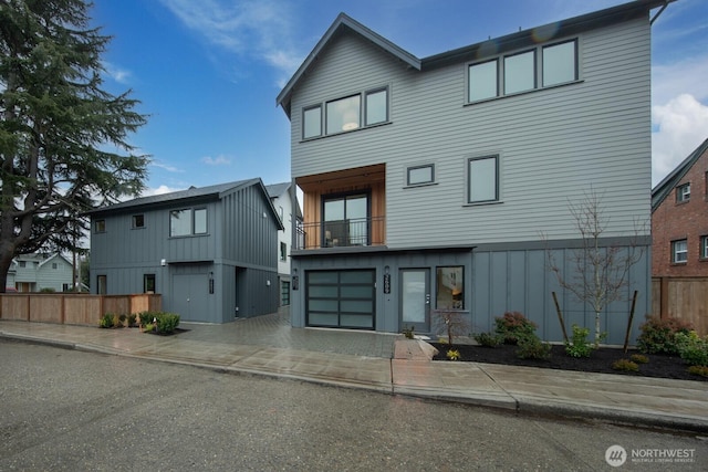 contemporary house with a garage, a balcony, fence, and board and batten siding