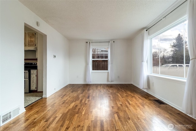 empty room featuring visible vents, a textured ceiling, and wood finished floors