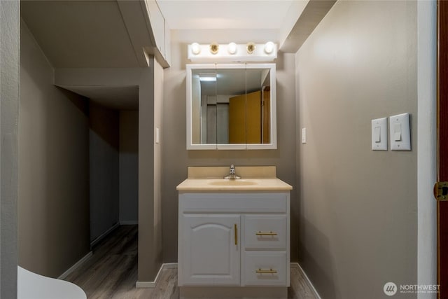 half bath featuring vanity, baseboards, and wood finished floors