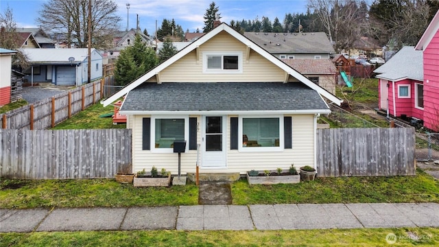 bungalow-style home featuring a residential view, a fenced backyard, a front lawn, and roof with shingles