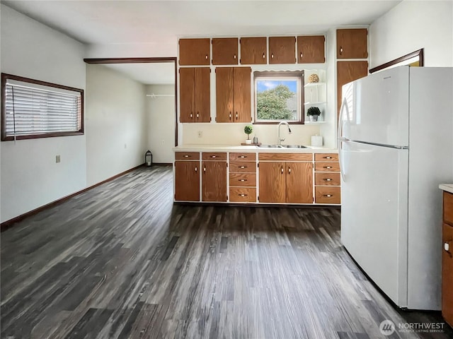 kitchen featuring brown cabinets, dark wood finished floors, light countertops, freestanding refrigerator, and a sink