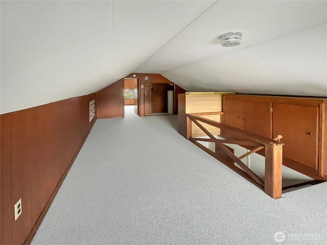 additional living space featuring light carpet, vaulted ceiling, and wood walls