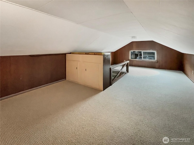 bonus room featuring lofted ceiling, wood walls, and light carpet