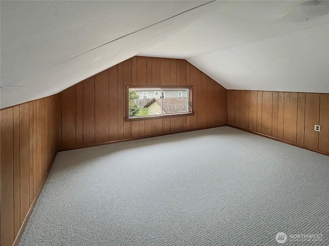 additional living space featuring vaulted ceiling, wood walls, and light colored carpet