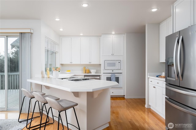 kitchen featuring light wood finished floors, white cabinets, a breakfast bar, stainless steel appliances, and light countertops