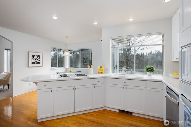 kitchen with stovetop with downdraft, a peninsula, a sink, light countertops, and stainless steel dishwasher