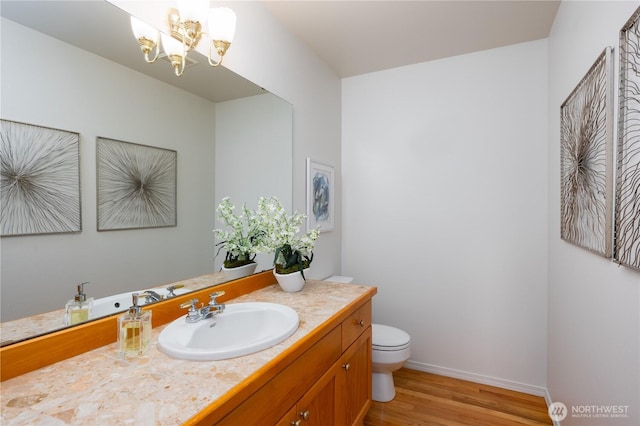 bathroom with toilet, an inviting chandelier, vanity, wood finished floors, and baseboards