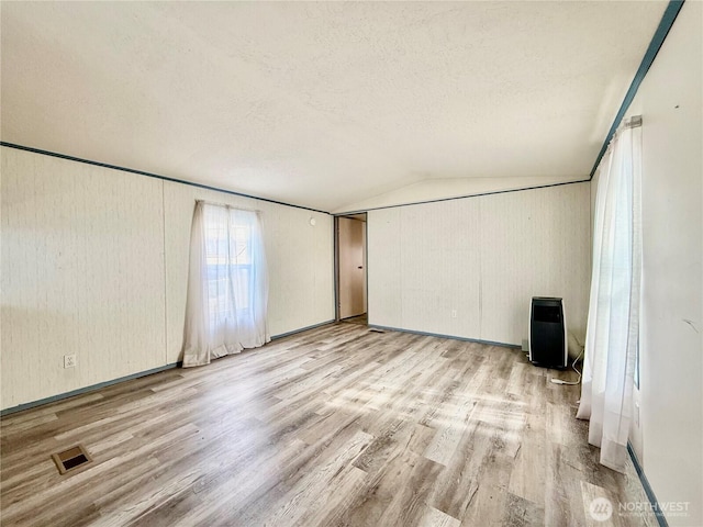 unfurnished room with vaulted ceiling, visible vents, light wood finished floors, and a textured ceiling