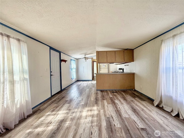 kitchen with light wood-type flooring, brown cabinets, a peninsula, a textured ceiling, and a ceiling fan