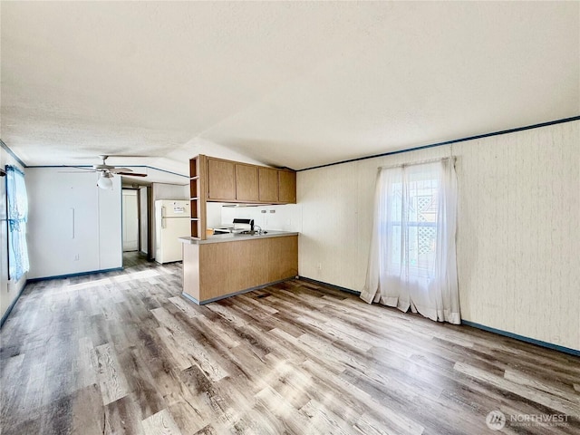 kitchen with brown cabinetry, wood finished floors, a peninsula, open shelves, and freestanding refrigerator