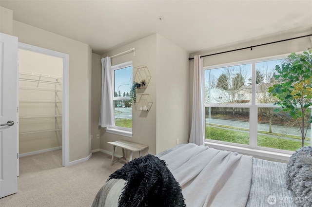 bedroom with baseboards, a walk in closet, and light colored carpet