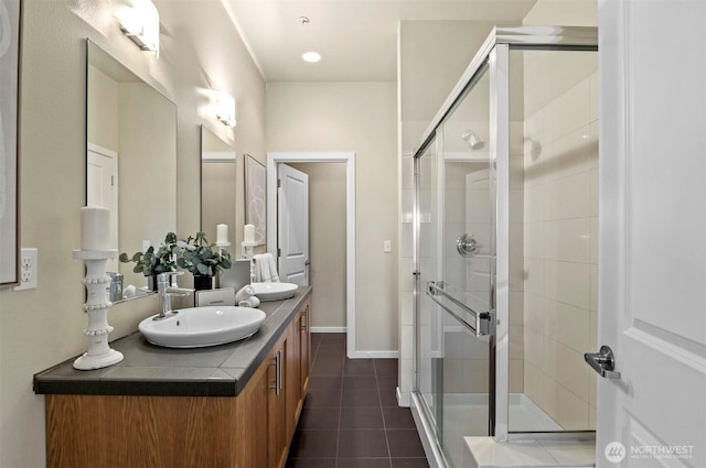 full bath featuring double vanity, baseboards, tile patterned flooring, a shower stall, and a sink