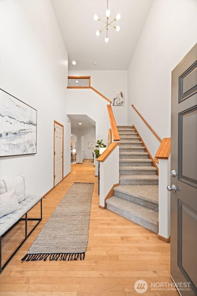 entryway with light wood finished floors, stairway, arched walkways, and an inviting chandelier