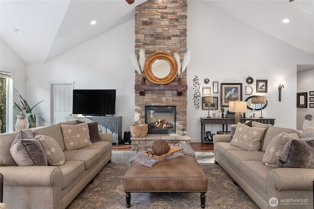 living room with recessed lighting, high vaulted ceiling, wood finished floors, and a stone fireplace