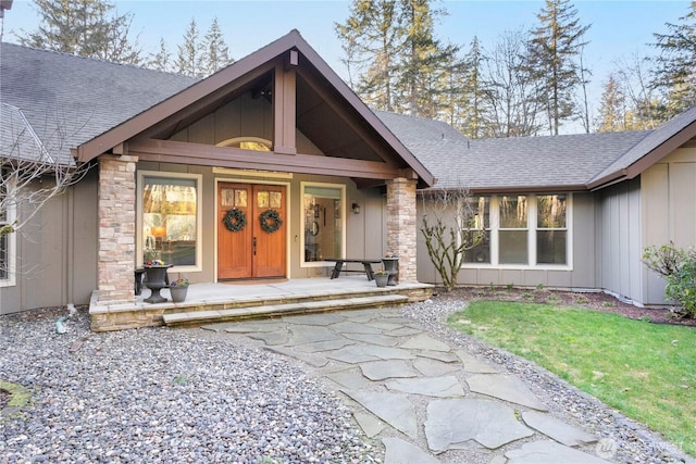 doorway to property featuring stone siding, a porch, roof with shingles, and board and batten siding