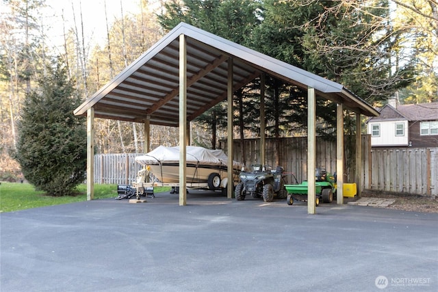 view of parking / parking lot with driveway, fence, and a carport