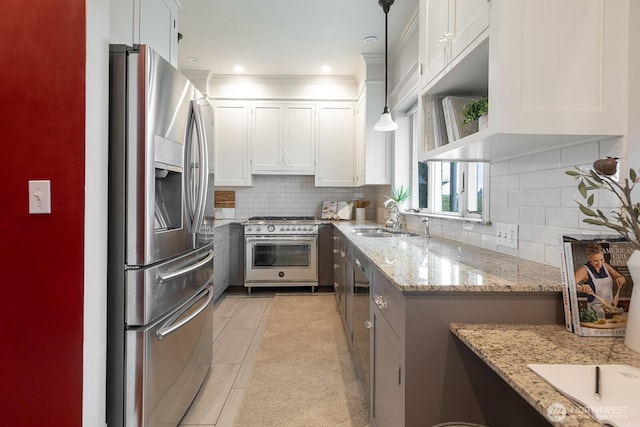 kitchen with appliances with stainless steel finishes, decorative light fixtures, light stone countertops, white cabinetry, and a sink