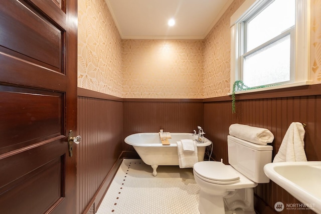 full bath featuring a freestanding tub, toilet, ornamental molding, wainscoting, and wallpapered walls