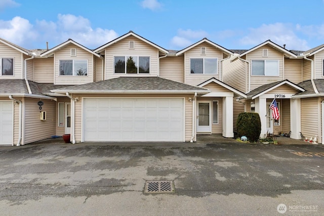 view of property with driveway, a garage, and roof with shingles