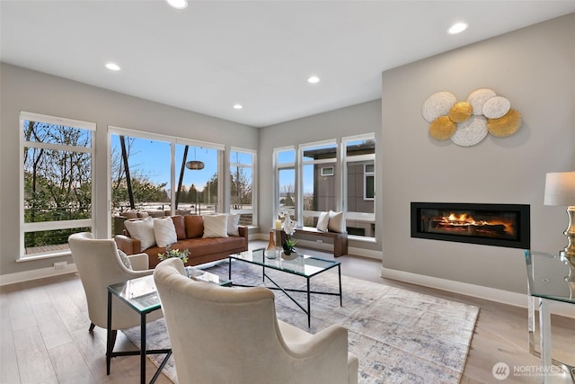 living room featuring a glass covered fireplace, light wood-style flooring, and recessed lighting