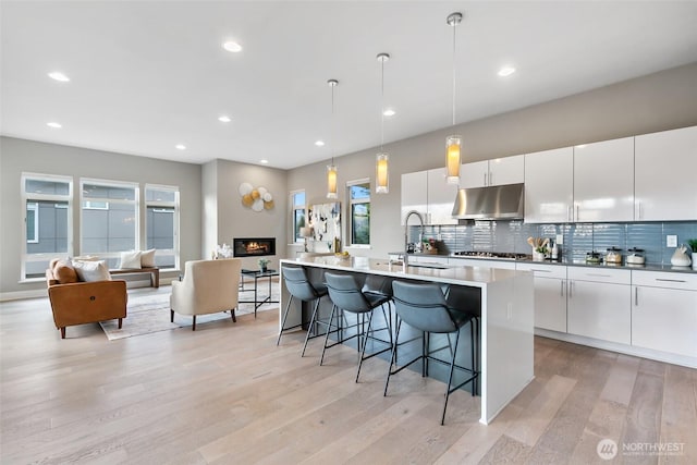 kitchen with pendant lighting, stainless steel gas cooktop, a breakfast bar area, white cabinetry, and under cabinet range hood