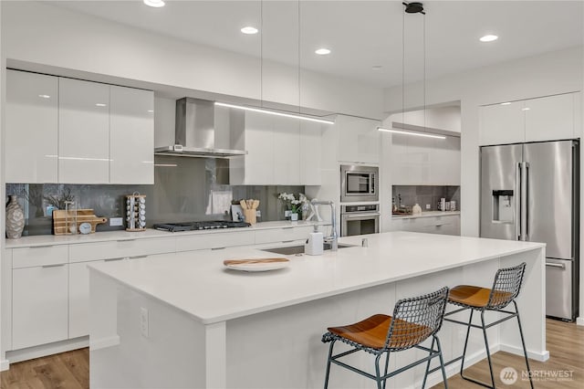 kitchen with light countertops, appliances with stainless steel finishes, white cabinetry, wall chimney range hood, and modern cabinets