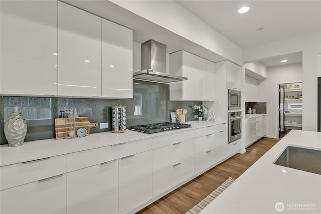 kitchen with white cabinets, wall chimney exhaust hood, modern cabinets, appliances with stainless steel finishes, and light countertops