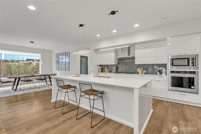 kitchen featuring modern cabinets, appliances with stainless steel finishes, decorative light fixtures, light countertops, and wall chimney range hood