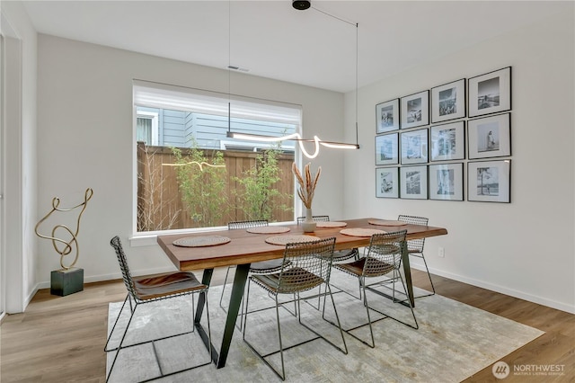 dining room with light wood finished floors, visible vents, and baseboards