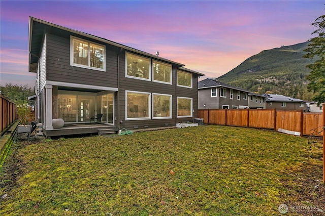 back of house at dusk featuring central air condition unit, a fenced backyard, a mountain view, and a yard