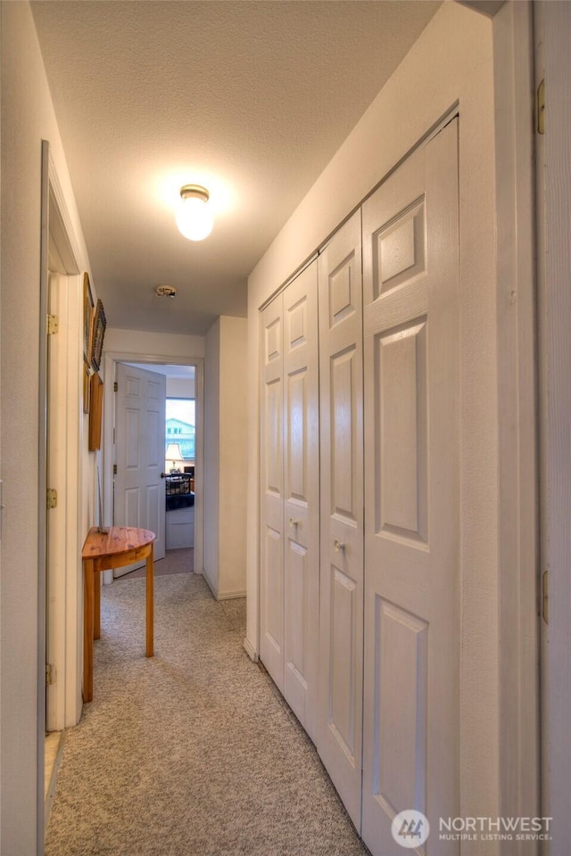 hallway with light carpet and a textured ceiling